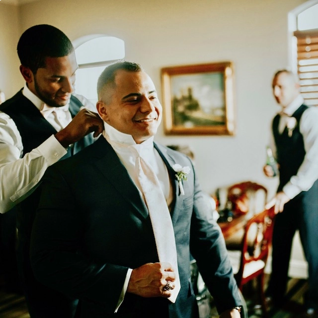 A man getting his suit jacket on while another man helps him get ready.