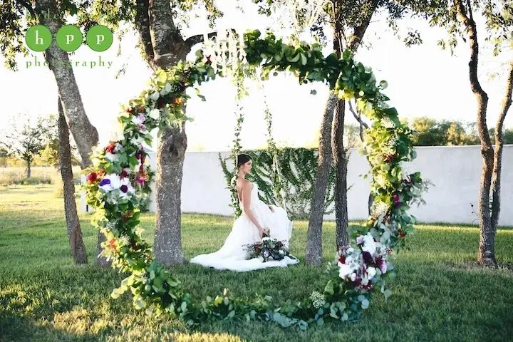 A bride sitting on the ground in front of trees.