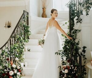 Bride on grand staircase with floral decor.